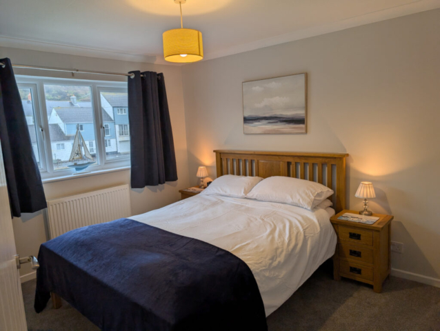 Master bedroom with king sized bed, white linen, blue throw, navy curtains, overlooking the harbour