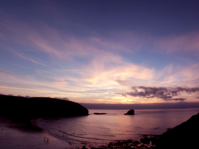 Sunset over Portreath Beach, with a calm sea and wispy clouds over the sea, lighting the sky in shades of blue and purple
